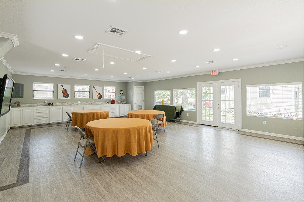 A spacious event hall with round tables covered in orange tablecloths and chairs, well-lit with natural and artificial lighting.