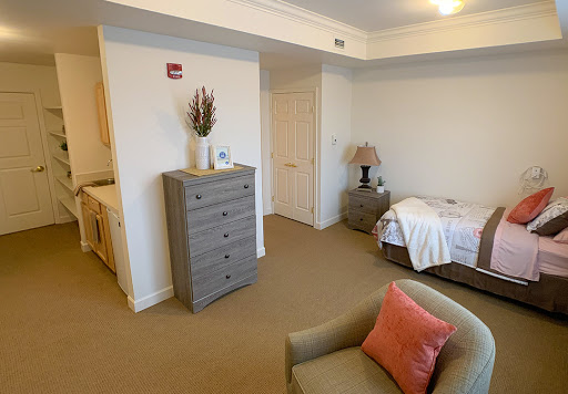 A cozy bedroom featuring a dresser, chair, and neatly made bed in a light and airy space.