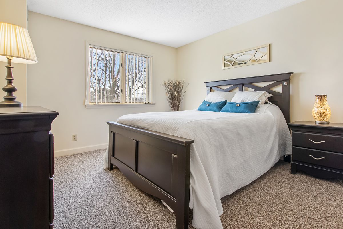 A modern bedroom with a large bed, white bedding, and decorative pillows, featuring a window that lets in natural light.