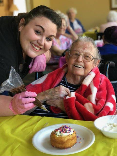 A caregiver and an elderly person smiling together, enjoying a cupcake.