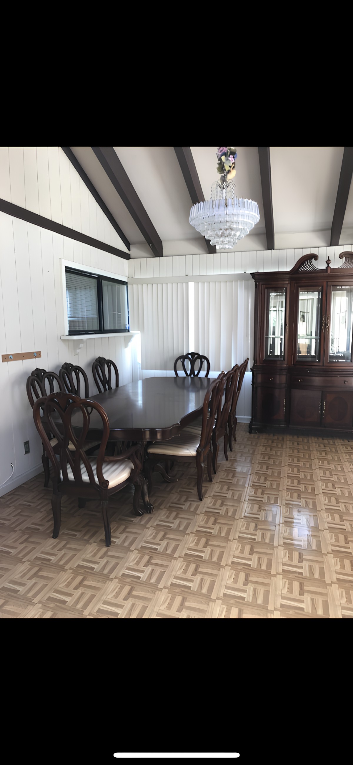 A dining room featuring a large wooden table with chairs, a chandelier, and a cabinet.