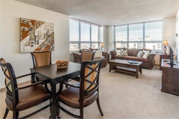A modern living room with an open dining area, featuring large windows and stylish furniture.