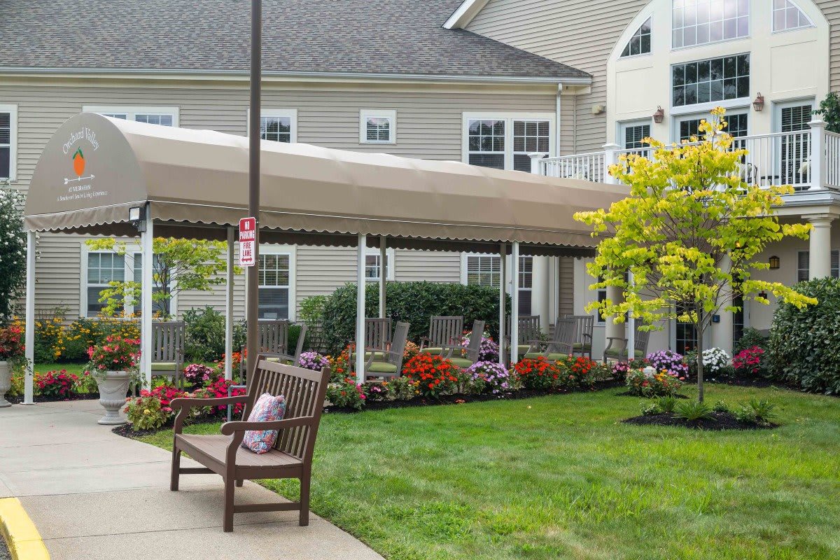 A peaceful garden area with a bench, canopy, and colorful flowers outside a building.