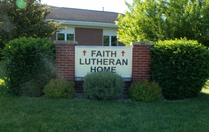 A brick sign for Faith Lutheran Home surrounded by greenery.