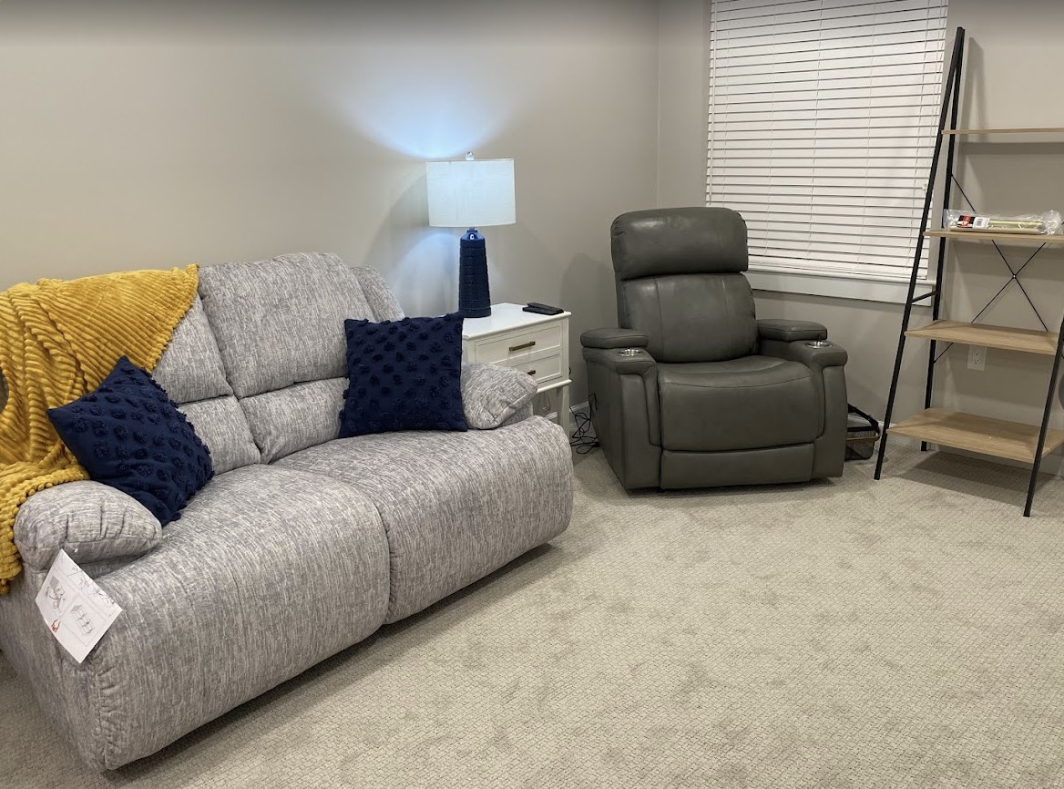 A cozy living room with a sofa, recliner, and a lit lamp.