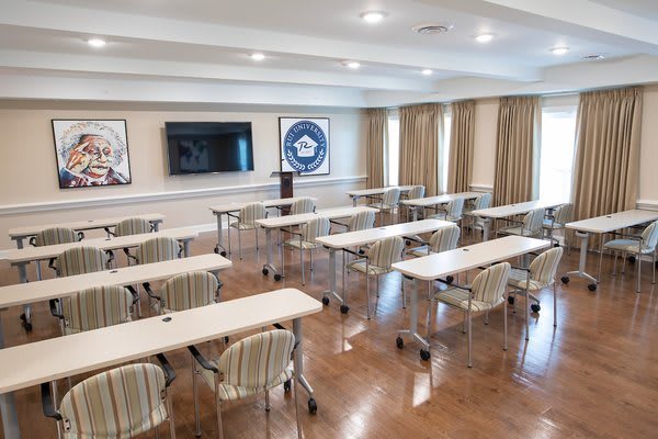 A modern conference room set up for meetings or classes, equipped with desks, chairs, and a large screen for presentations.