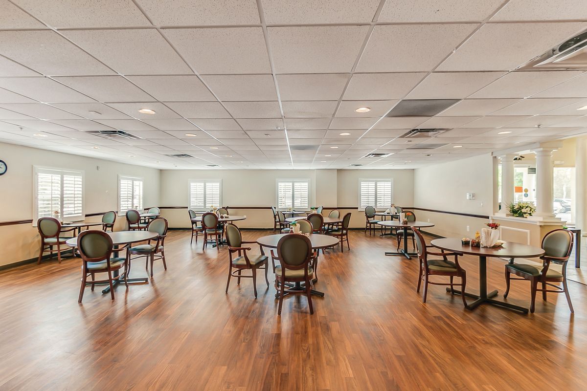 An empty dining room with hardwood floors, arranged tables and chairs, and windows letting in natural light.