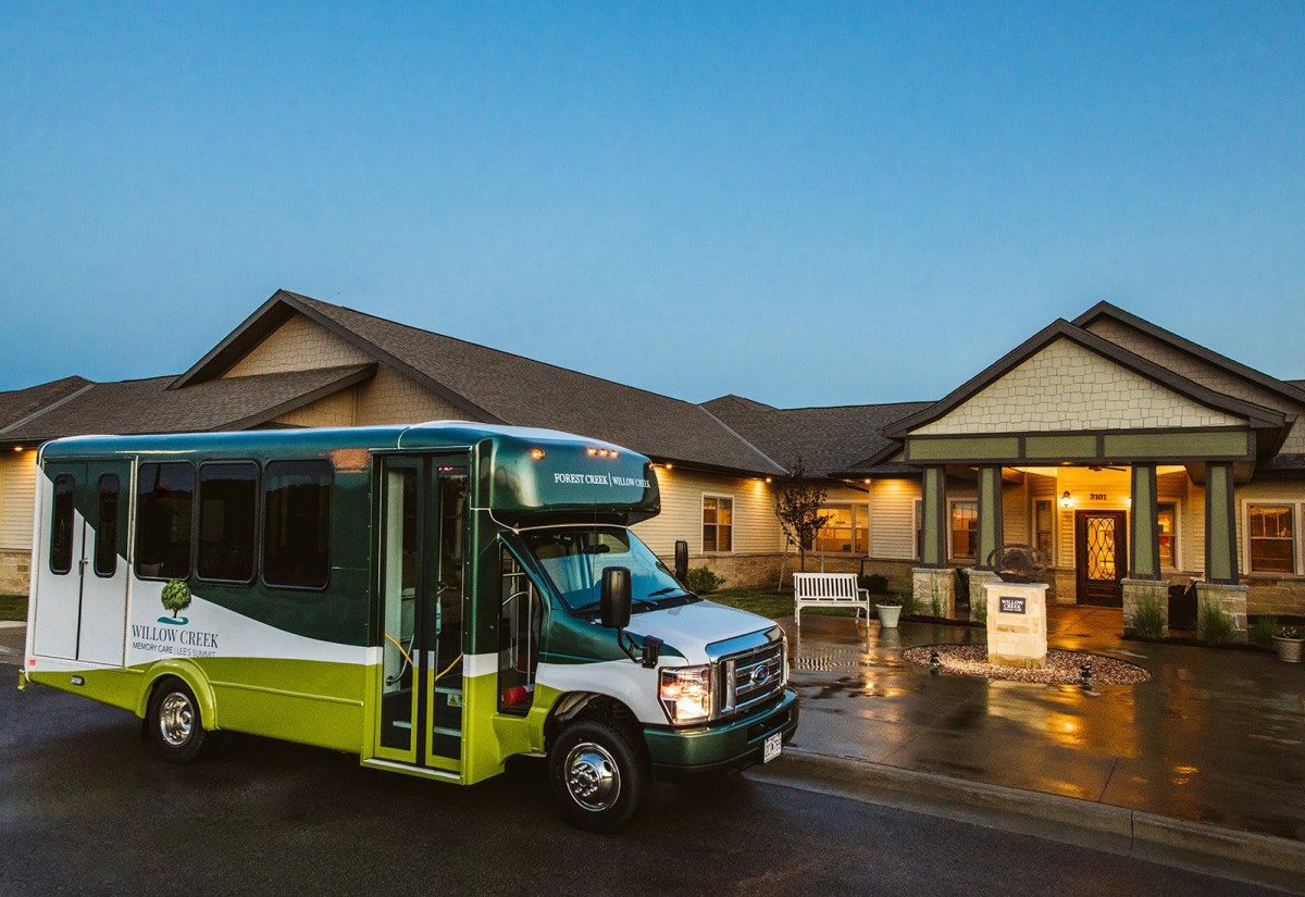 A green and white bus parked outside a building in the evening.