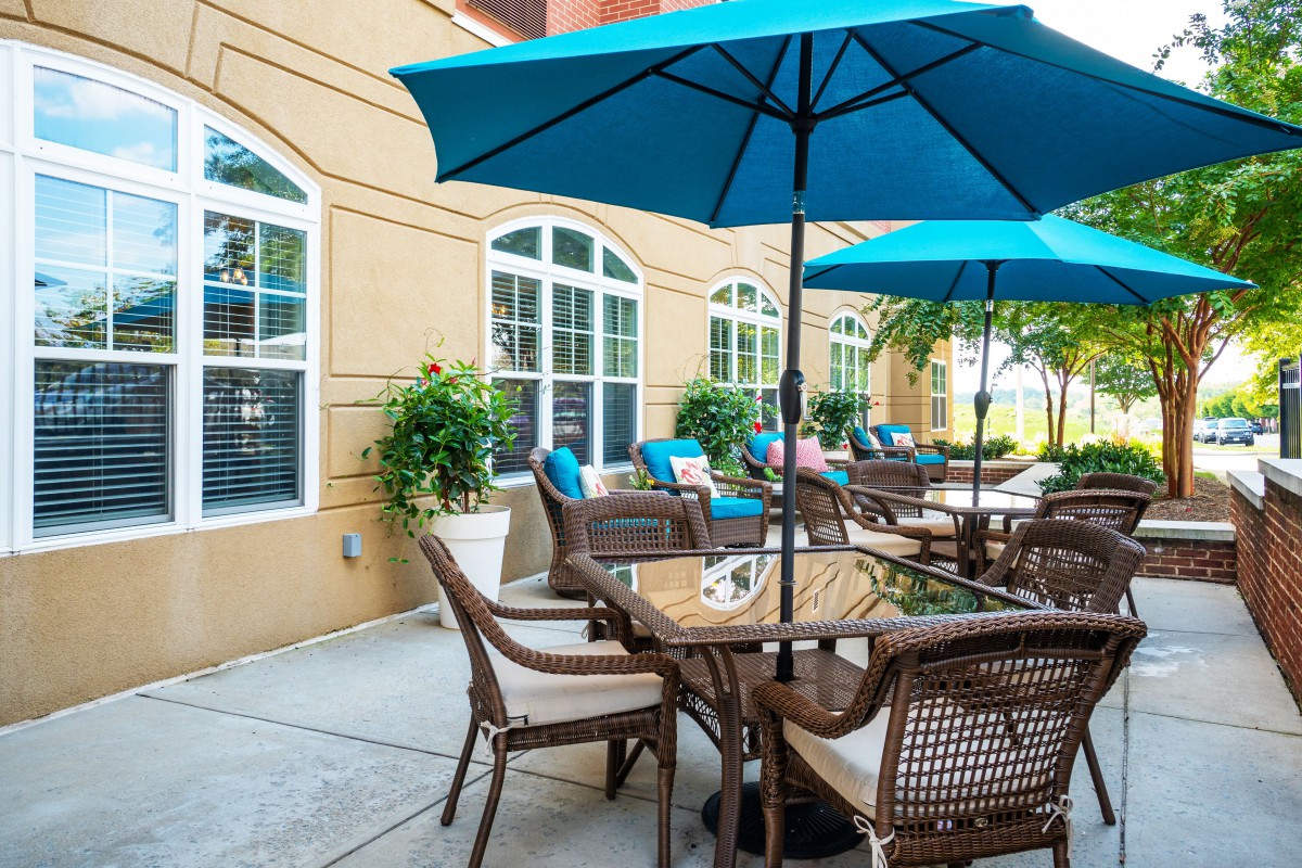An outdoor patio area with tables, chairs, and blue umbrellas alongside a building.