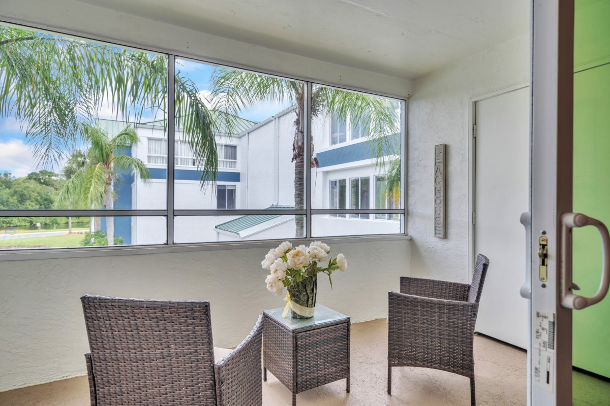 A cozy patio with wicker chairs and a small table adorned with flowers, overlooking palm trees.