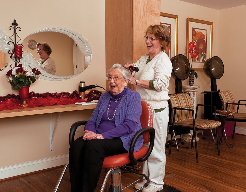 An elderly woman enjoys a haircut at a cozy hair salon, smiling as the stylist works.