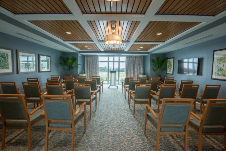 A well-organized conference room with rows of chairs facing a podium, featuring elegant ceiling designs and abundant natural light.