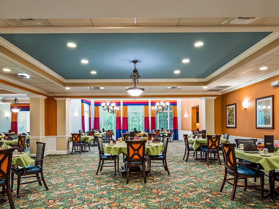 A brightly decorated dining room with multiple tables and chairs, featuring chandeliers and colorful curtains.