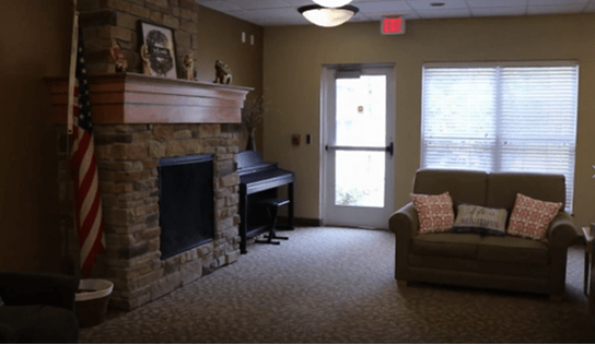 A cozy living room with a stone fireplace, piano, and sofa.