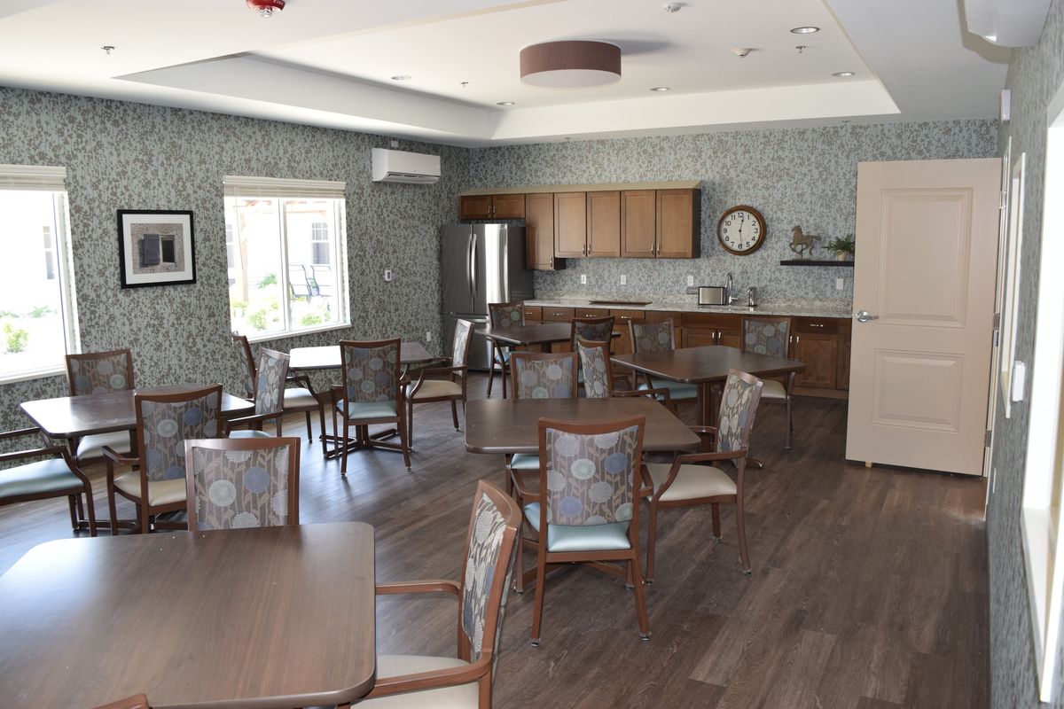 A cozy dining room with wooden tables and chairs, featuring a kitchenette and a wall clock.