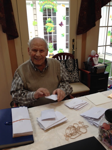 An elderly man enjoys a crafting session, folding envelopes at a bright and cheerful table.
