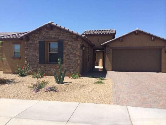 A single-story brick house with a desert landscape and attached garage.
