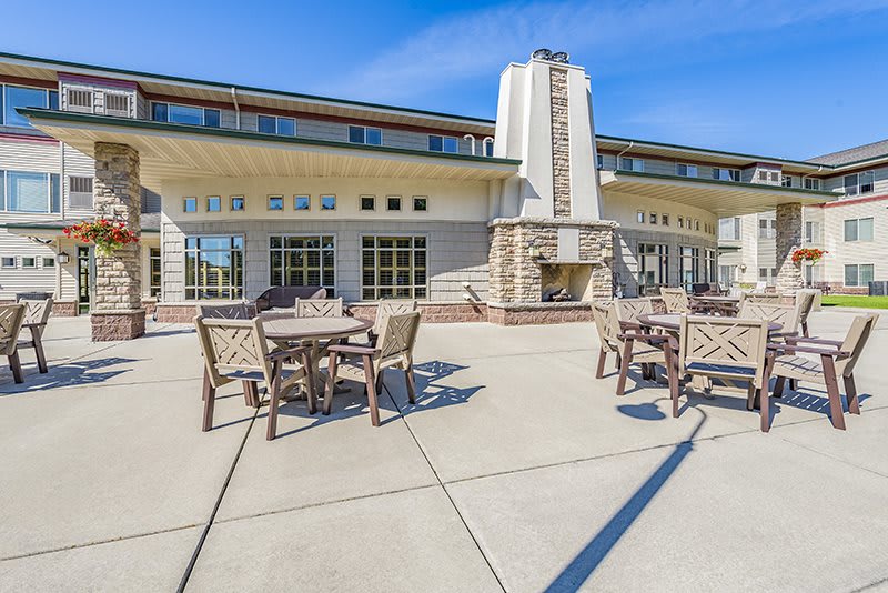 A spacious outdoor patio with tables and chairs set against a large, modern building under a clear blue sky.