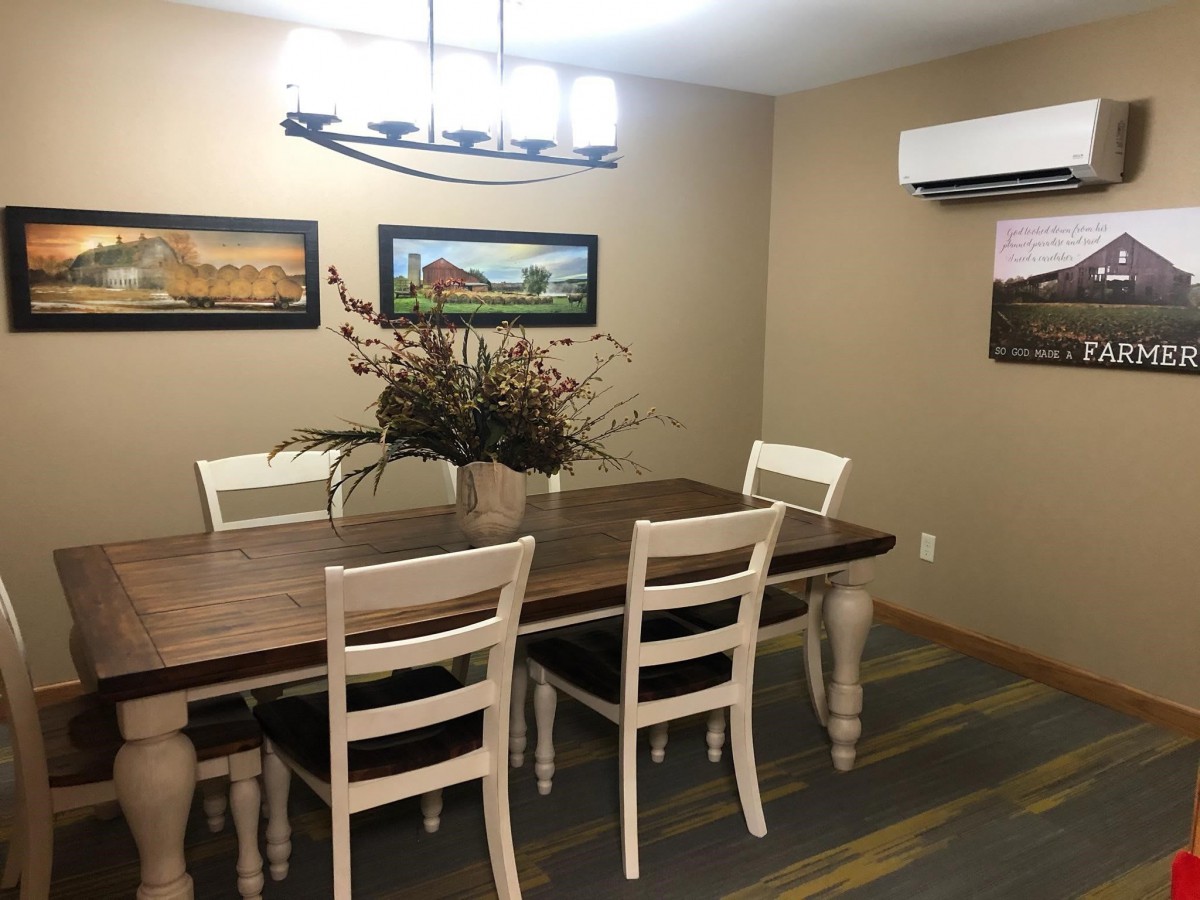 A cozy dining room with a wooden table and six chairs, adorned with wall art and a central plant decoration under modern lighting.