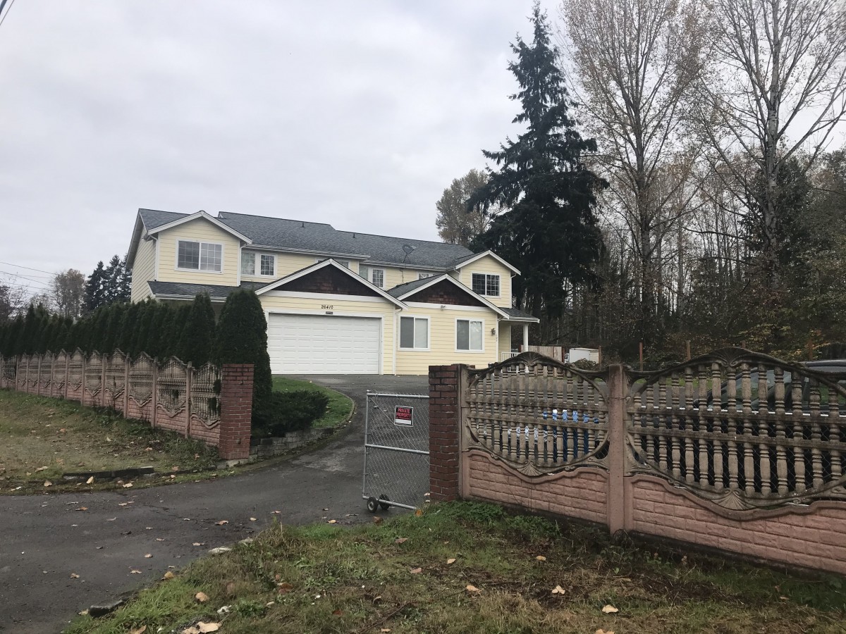 A two-story house with a fenced driveway on a cloudy day.