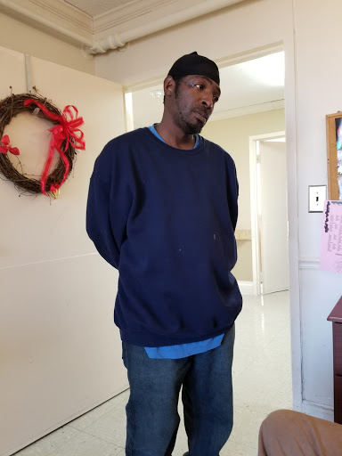 A man standing indoors, wearing a dark sweatshirt and jeans.
