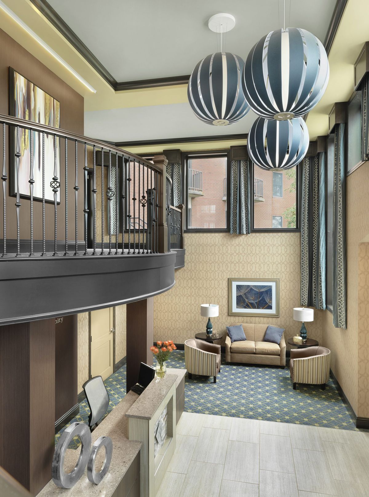 A modern lobby interior featuring a seating area, decorative lighting fixtures, and an upper-level balcony.