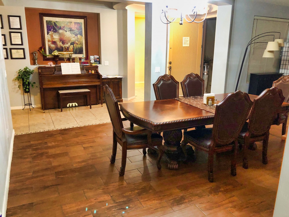 A cozy dining room with a wooden table and chairs, a piano, and a decorative chandelier.