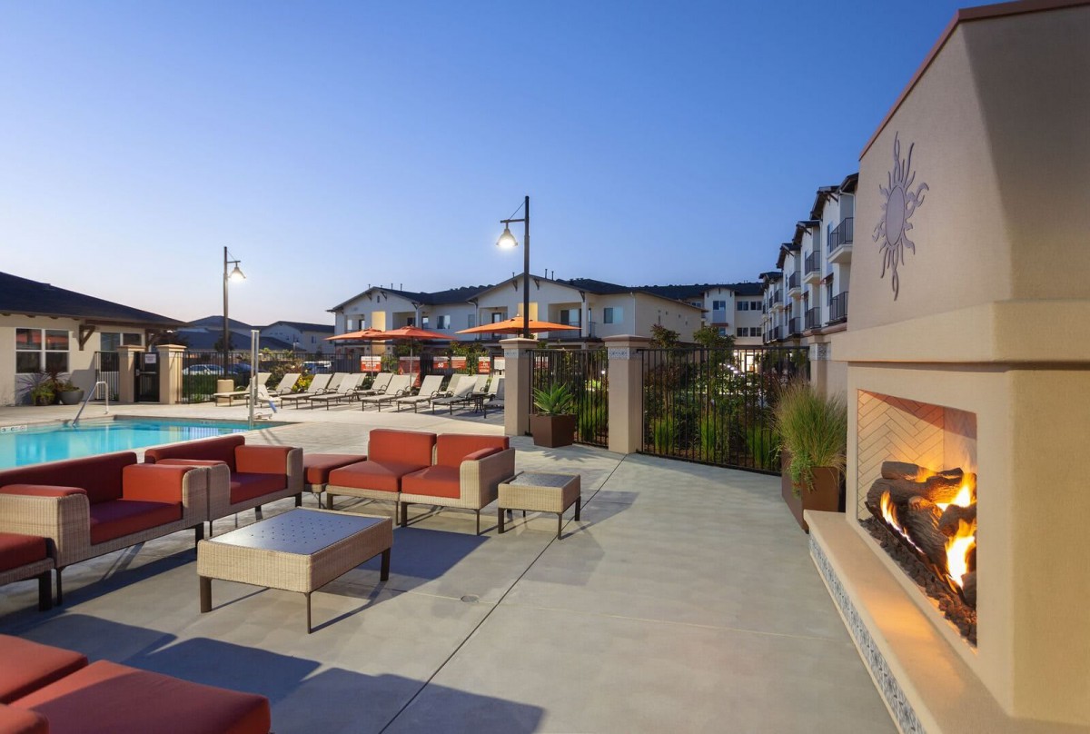 An outdoor seating area with a view of a pool at an apartment complex in the evening.