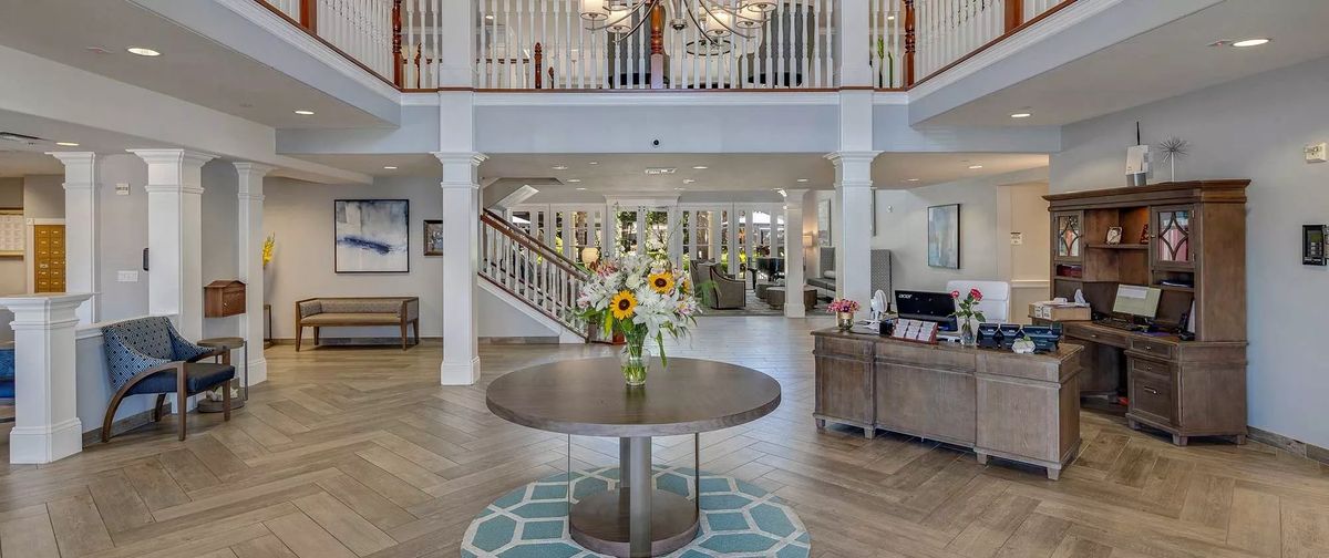A spacious and elegantly decorated lobby with a central table adorned with flowers and a grand chandelier overhead.