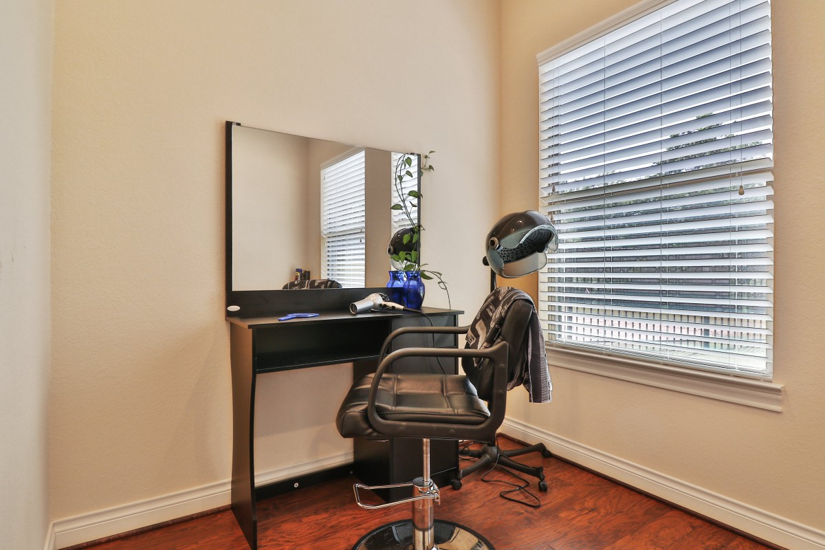 A minimalist hair salon setup featuring a styling chair, mirror, and hair dryer next to a window with blinds.
