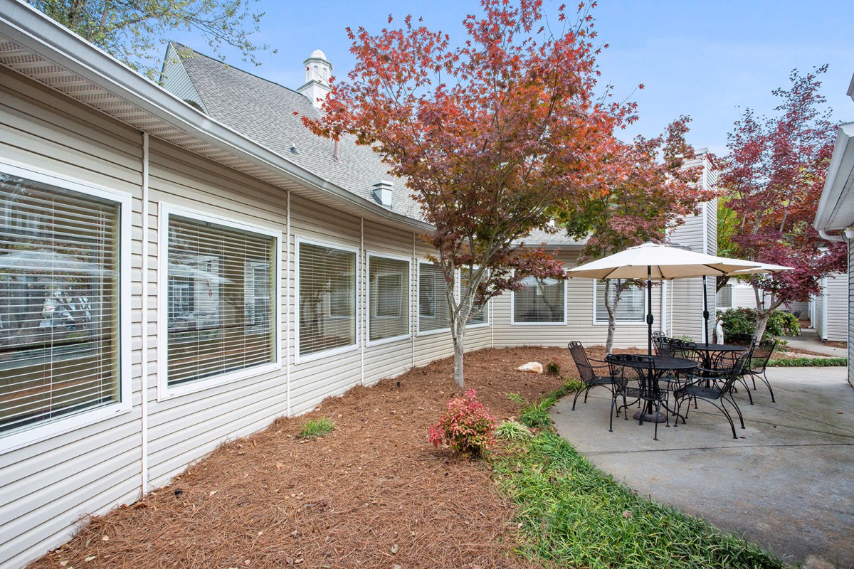 A peaceful patio area with outdoor seating and a tree with autumn foliage, adjacent to a building.
