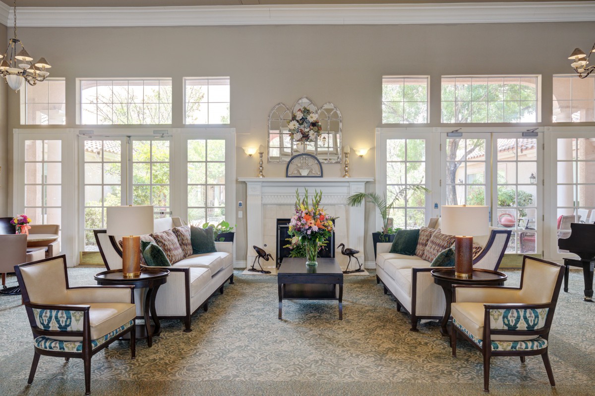 A spacious and elegant living room with large windows, cozy sofas, a central coffee table, and a decorative fireplace.