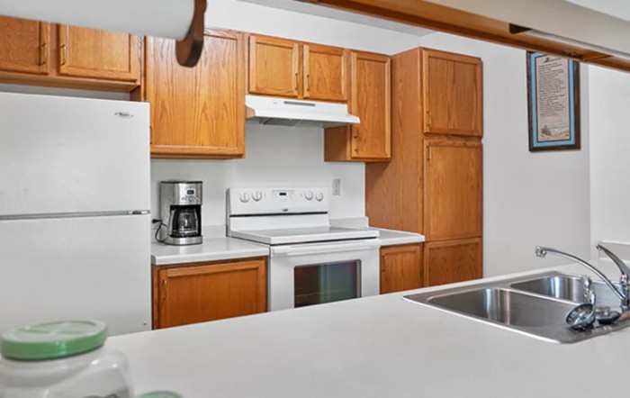 A modern kitchen with wooden cabinets, a white countertop, and essential appliances including a stove, oven, and coffee maker.