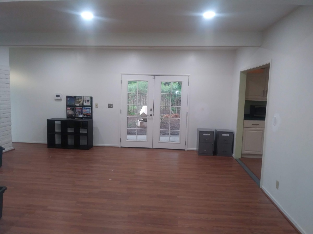 A spacious living room with wooden flooring, minimalist decor, and French doors leading outside.