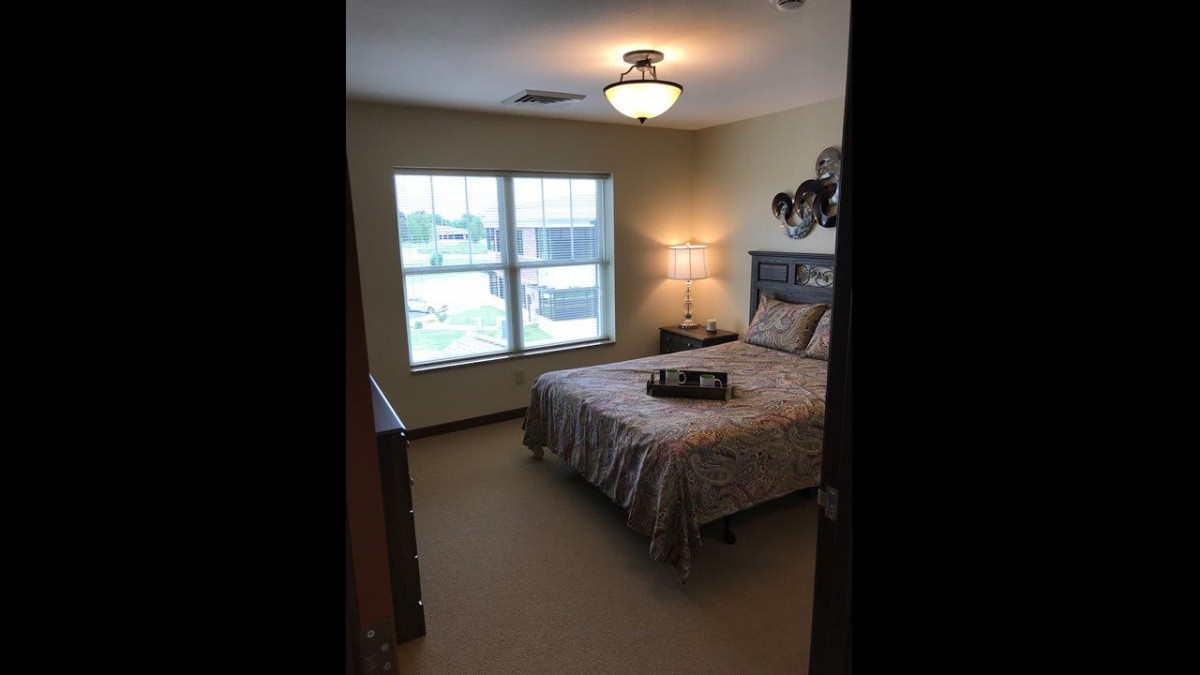 A cozy bedroom with a bed, lamp, and large window allowing natural light.