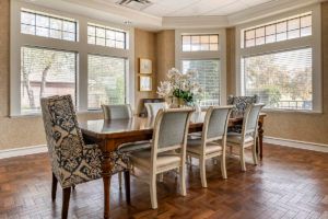 A beautifully arranged dining room with a wooden table, cushioned chairs, and large windows allowing ample natural light.