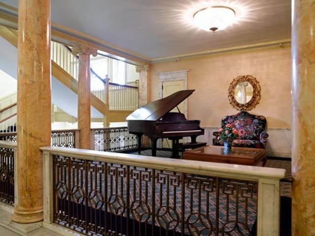 A beautifully designed interior featuring a grand piano, ornate furniture, and a decorative mirror next to a staircase.