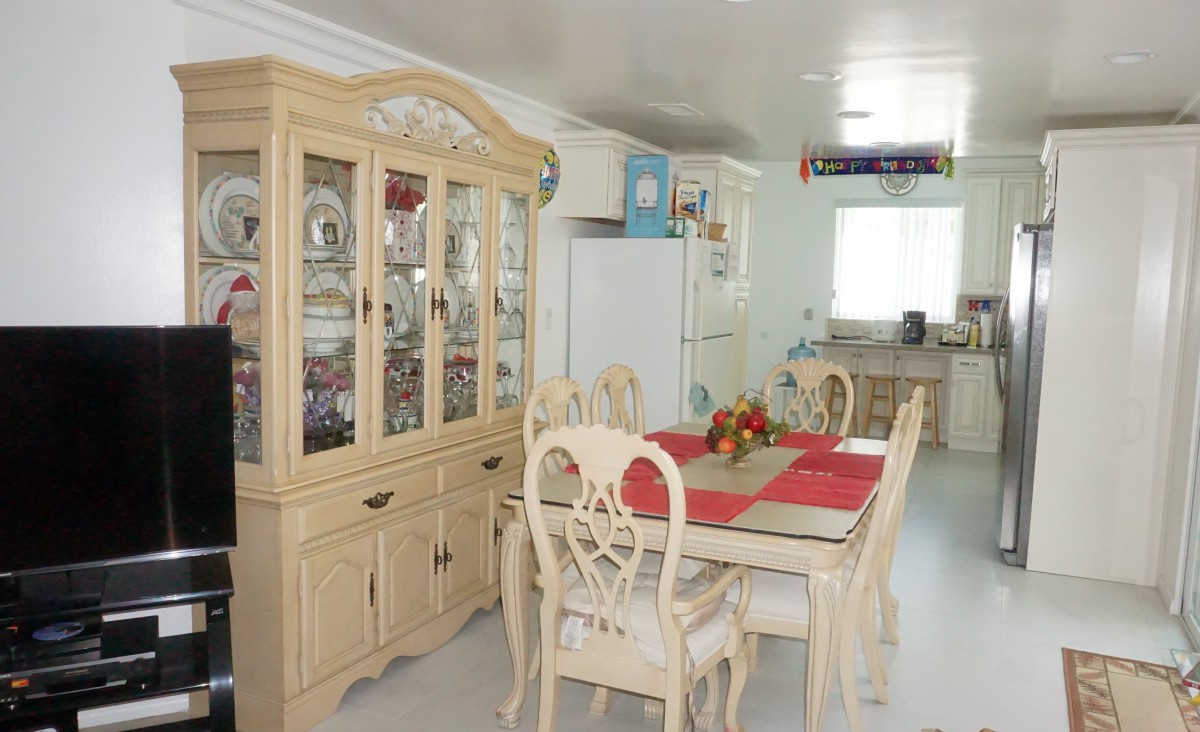 A bright dining area featuring a wooden dining table with red placemats and matching chairs, next to a glass-fronted cabinet filled with dishes.