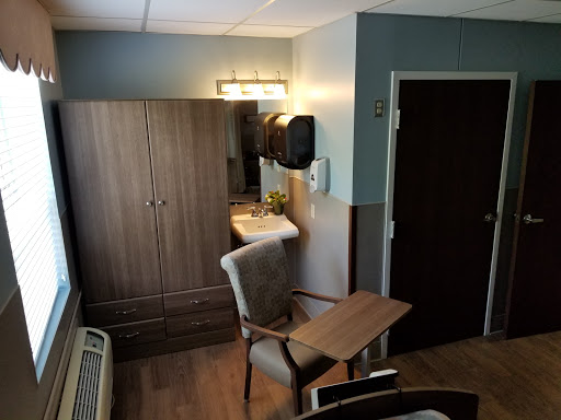 A cozy and functional room setup featuring a chair, table, wardrobe, and wash area.