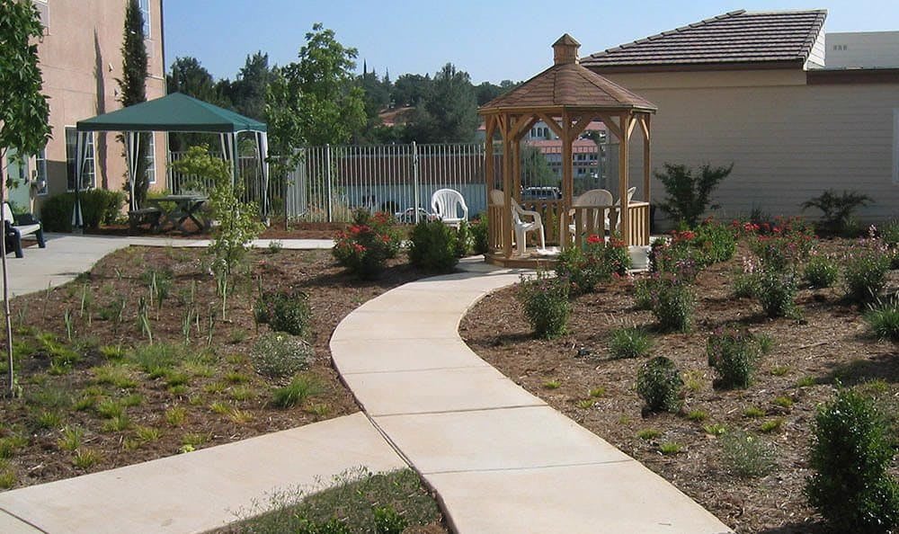 A garden pathway leading to a gazebo with chairs, surrounded by landscaping.