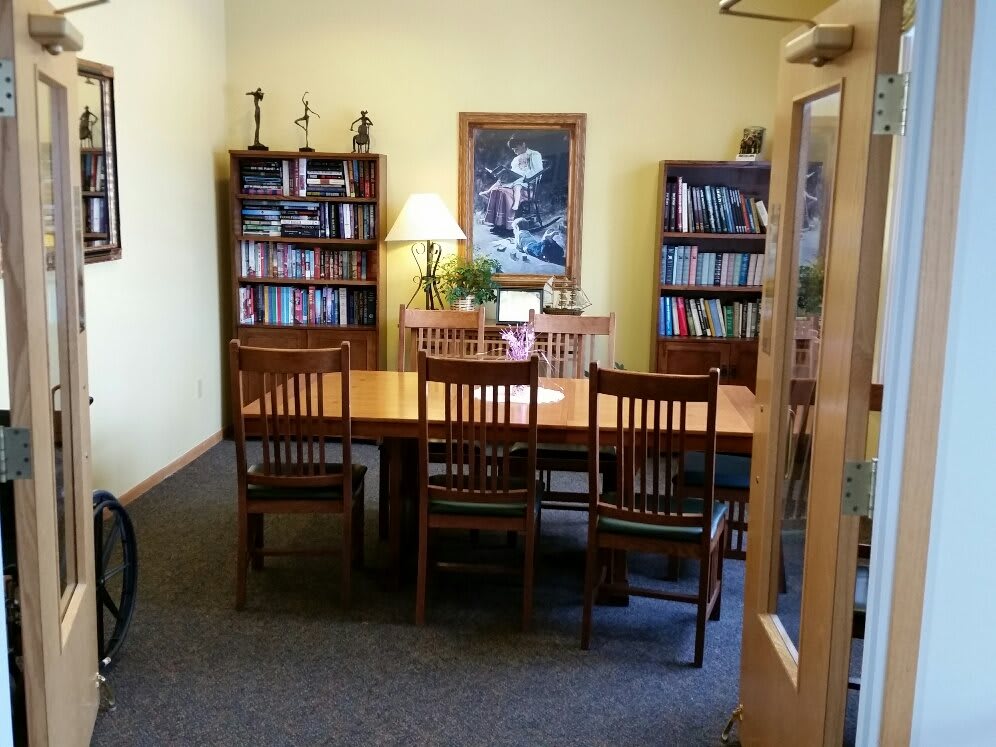 A cozy office meeting room with bookshelves and a central wooden table surrounded by chairs.