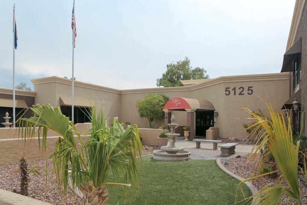 A beige building with an entrance featuring a red canopy, surrounded by landscaping and a fountain in front.