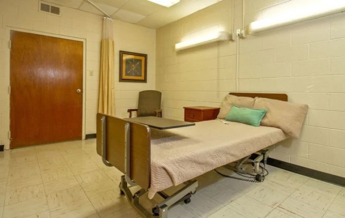 A hospital room with a single bed and simple furnishings.