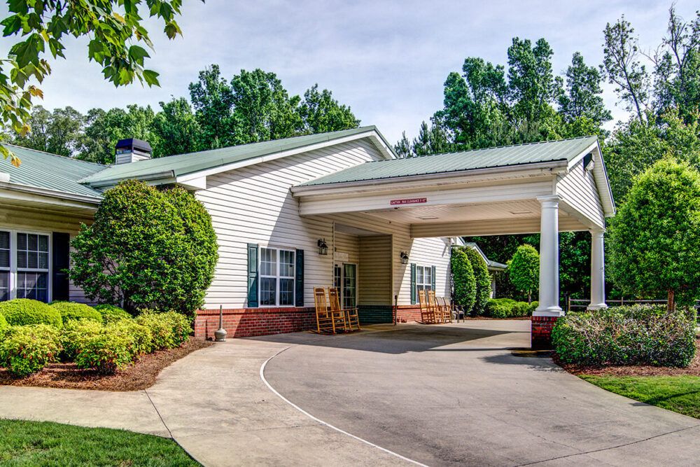 A view of a building entrance with a covered driveway and surrounding greenery.
