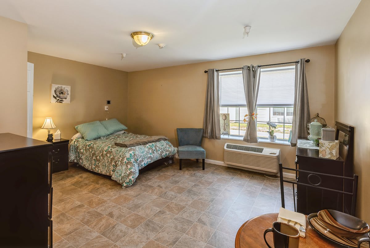A cozy bedroom with a bed, chair, and table next to large windows.