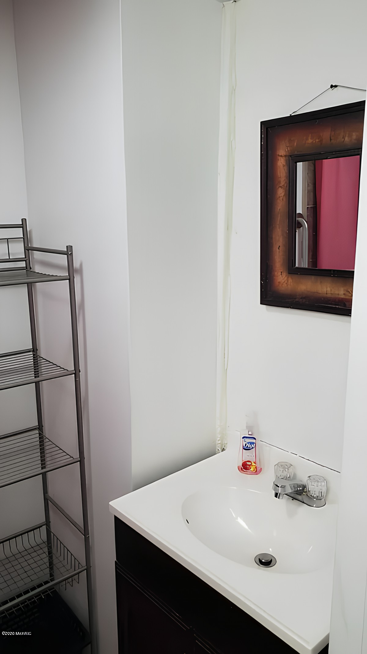 A minimalist bathroom setup featuring a sink, mirror, and metal towel rack.