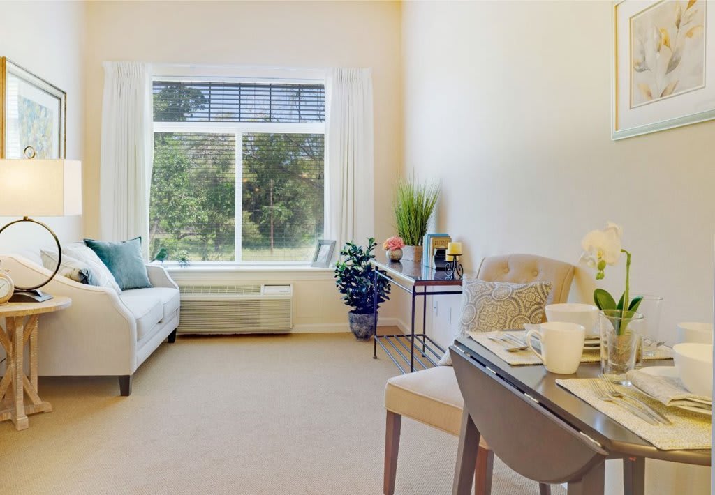 A bright and cozy living room with a large window, sofa, and dining area.