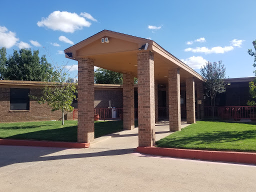 A well-structured brick building with a covered entrance, surrounded by green grass and under a clear blue sky.