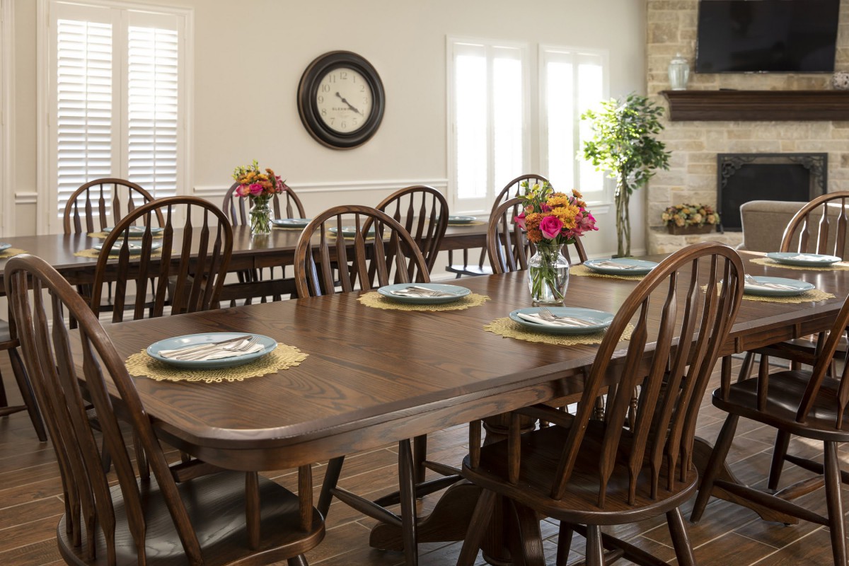 A dining room with wooden tables and chairs, decorated with place settings and flower arrangements.