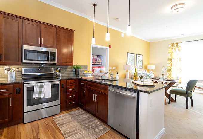 A modern kitchen with stainless steel appliances and wooden cabinets, featuring an island countertop and pendant lighting.